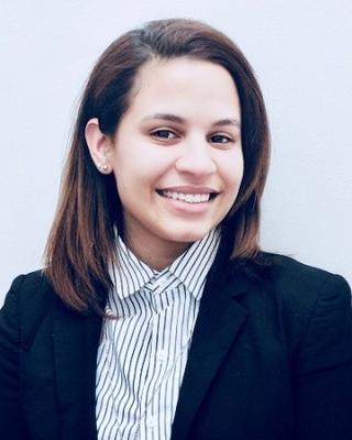 Janelle Batista, smiling, with long dark hair, striped button down, dark blazer, and light grey background