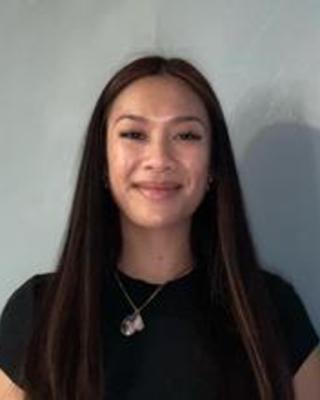 Jasmine Khlieng with long dark hair, black top, blue-grey background