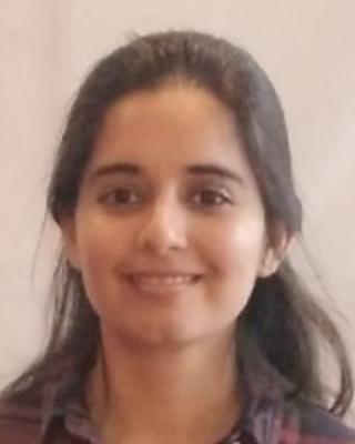 Jenia Singh with long dark hair pulled partway back, wearing red plaid shirt, in front of beige background
