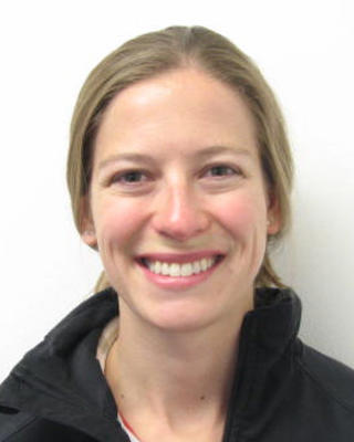 Jennifer Delaney, smiling, long blond hair pulled back, wearing black coat, white background 