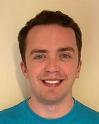 Jordan Johnson with short brown hair and a teal shirt, in front of a beige background