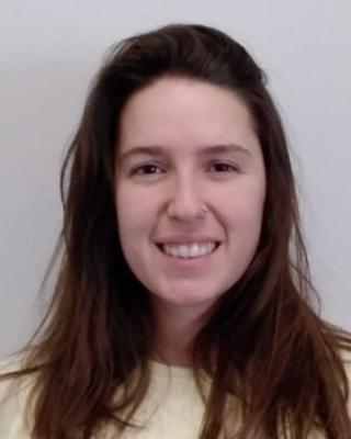 Julia Chaumel Cerda with long brown hair, light yellow shirt, grey background