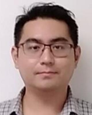 Karma Nanglu with short black hair, glasses, and check shirt, in front of white background