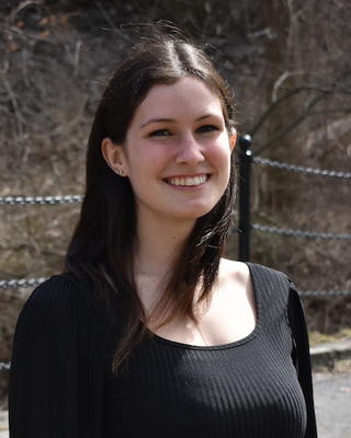 Kelsie Lopez with long brown hair and a black top, in front of bare branches and walkwayfence
