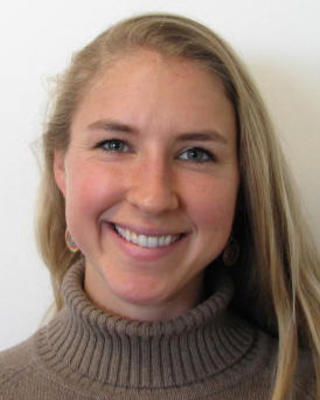 Kiah Hardcastle with long blonde hair, taupe turtleneck sweater, white background