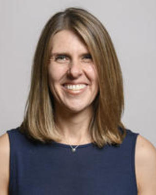 Kristin Pennarun with long dark blond hair, sleeveless blue top, light grey background