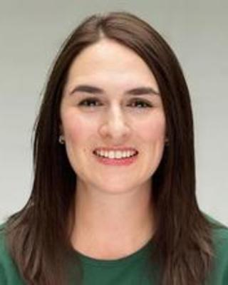 Laura Ostrowsky with long brown hair, wearing a green top, in front of grey background