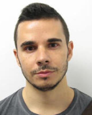 Luis Quijada Fumero with short dark hair and beard, wearing a grey shirt, in front of white background