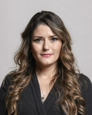 Melinda Peterson with long wavy brown hair, black sweater, light grey background