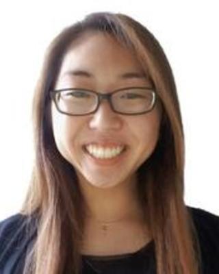 Melissa Mai with long brown hair, glasses, and a dark top, in front of a white background