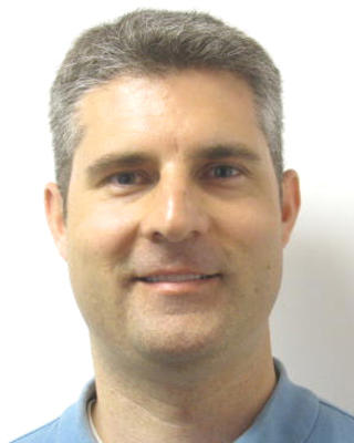 Michael Butts, smiling, with short grey hair, light blue polo, cream background