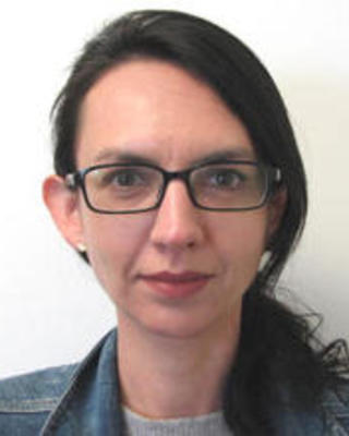 Natalia Pabon Mora with long dark hair pulled back, wearing glasses and a denim jacket, in front of a white background