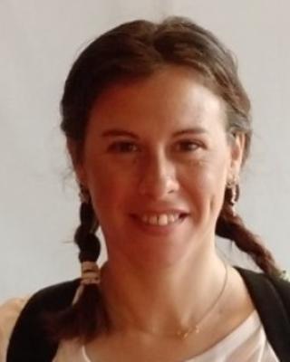 Paula Rodriguez Flores with hair in two long braids, white top, and backpack straps, in front of light grey background