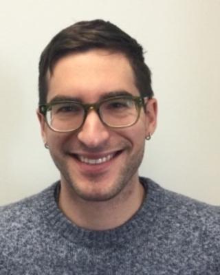 Peter Flynn with short brown hair, dark glasses, blue and white sweater