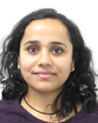 Ramya Purkanti with long dark curly hair, wearing a purple top, in front of a white background