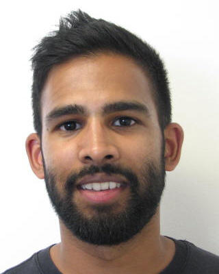 Robin Thandiackal with short black hair and beard, wearing a dark shirt, in front of a white background