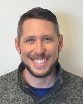 Ryan Bos with short brown hair, grey fleece, in front of white background