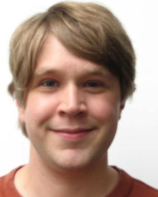 Ryan Maloney with short dark blonde hair, wearing a red-orange shirt, in front of a white background