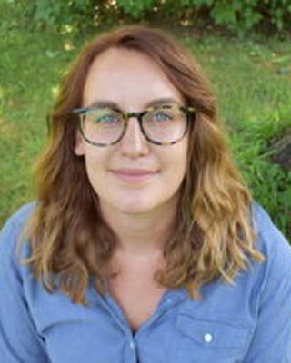 Sarah Losso with long wavy hair, dark glasses, blue button down shirt, grass in background