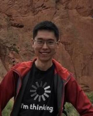 Shuonan He iwth dark hair, glasses, black t-shirt, red jacket, in front of red stone formation