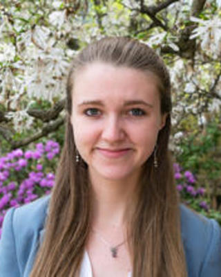 Sophie Everbach with long brown hair and a blue blazer, in front of white and purple flowering tree and shrubs