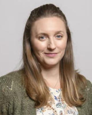 Stephanie Pierce with long, blonde hair wearing a green sweater, patterned shirt, in front of grey background 