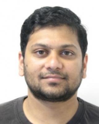 Tarun Kumar with short dark hair and beard, wearing a dark shirt, in front of a white background
