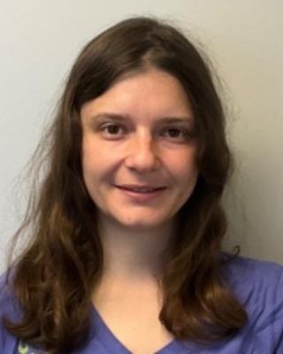 Teresa Pegan with long brown hair and blue top, with light grey background