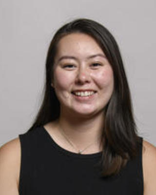 Tiara Borneman - smiling with long dark hair, black sleeveless shirt, grey background