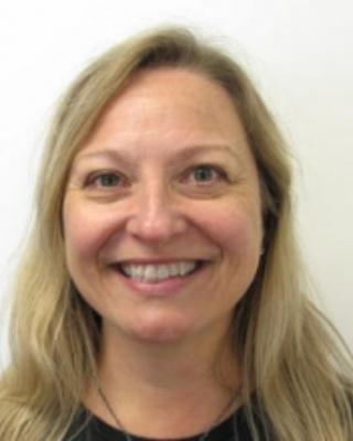 Wendy Heywood, smiling, with long blonde hair, dark top, white background