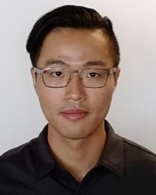 Yangfan Zhang with short black hair, glasses, and black shirt, in front of light grey background