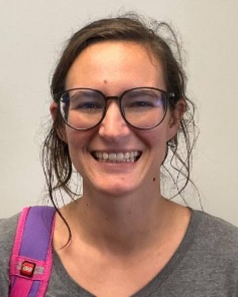Juli Cosgrove with wavy brown hair, glasses, and a grey top, in front of a light grey backgrond