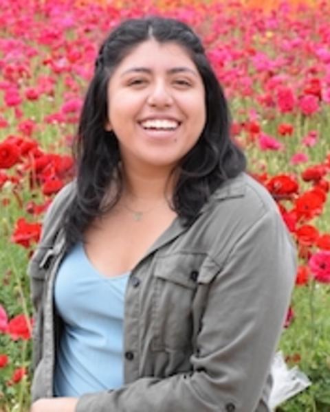 Adriana Aguilar-Maldonado with long dark hair, blue top and grey jacket, in a field of red flowers