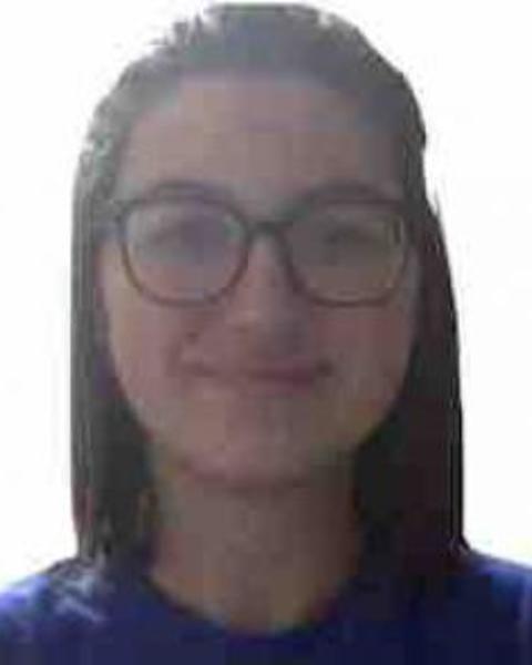 Maddi Waskom with long dark hair, wearing glasses and a blue top, in front of a white background