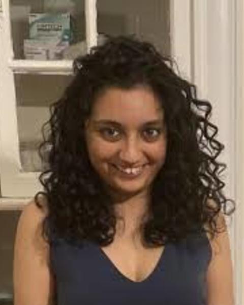 Shraddha Lall with long, curly dark hair, wearing blue sleevless top, in front of whitecabinet