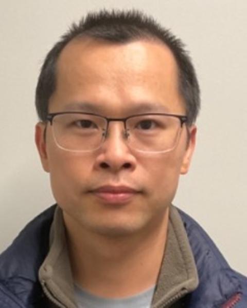 Bifeng Wu with short dark hair, wearing glasses and a blue coat, in front of a beige background