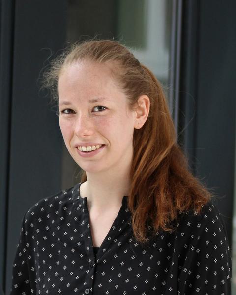 Jessica Stock with long red hair and a black top, in front of dark building