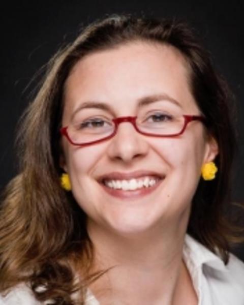 Amie Jones smiling with long brown hair, red glasses, white shirt, black background