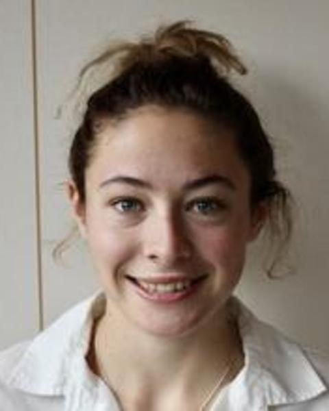 Arianna Lord with brown hair pulled up, a white top, in front of a beige wall