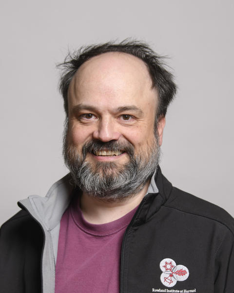 Benjamin de Bivort with beard and mustache wearing a red shirt and black jacket smiling