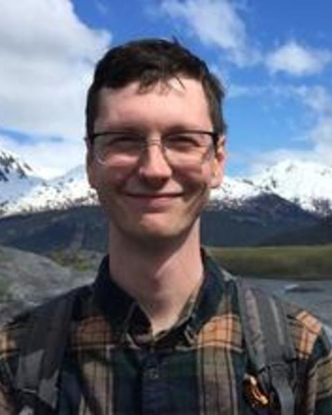 Calvin Heslop with short brown hair and glasses, wearing a plaid shirt, in front of distant snowy mountains