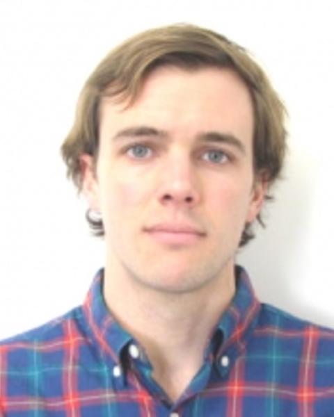 Daniel Hoer with short light brown hair, wearing a blue and red plaid shirt, in front of a white background