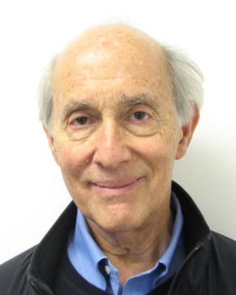Eric Chivian with short grey hair, a blue shirt, and dark coat, in front of a white background