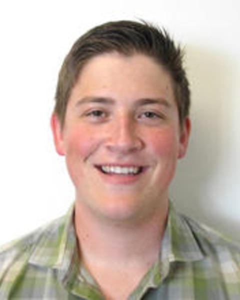 Evan Hockridge with short brown hair and a green plaid shirt, in front of a white background