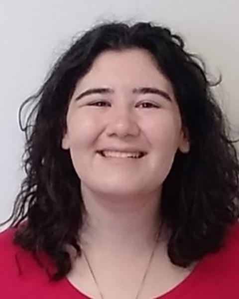 Isobel Ronai smiling, with long wavy dark hair, a red top, in front of beige background