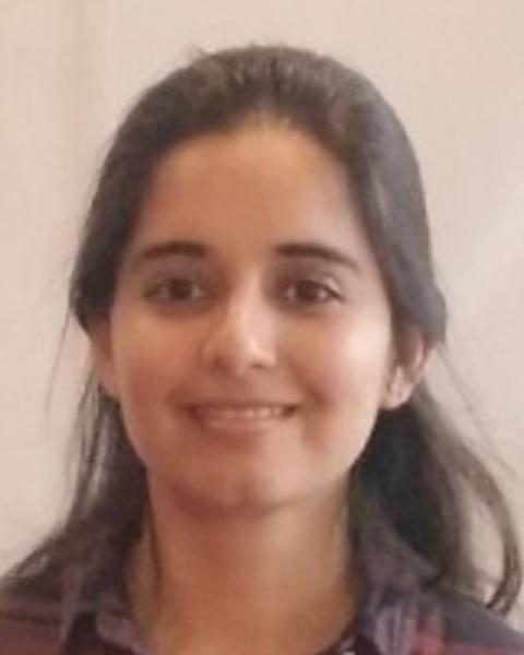Jenia Singh with long dark hair pulled partway back, wearing red plaid shirt, in front of beige background