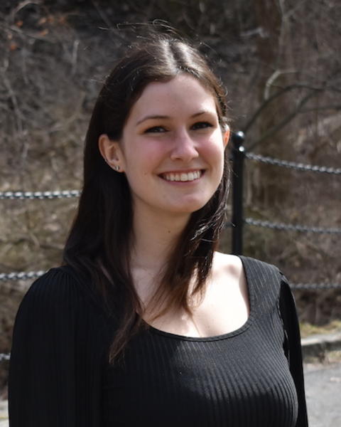 Kelsie Lopez with long brown hair and a black top, in front of bare branches and walkwayfence