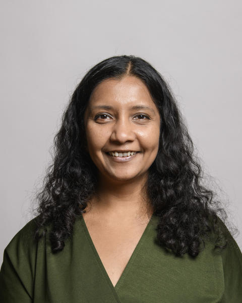 Mansi Srivistava with long, brown hair wearing a green blouse, in front of grey background
