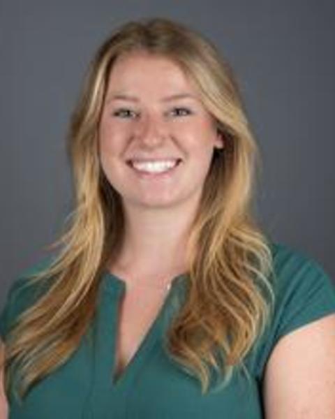 Nicole Adams - with long blond hair, short sleeved green shirt, and dark grey background