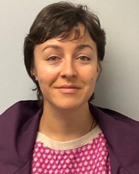 Petra Kovacikova with short brown hair, wearing pink shirt with white dots, purple coat, grey background